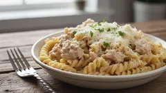 Tonnikalapasta lautasella, päällä juustoa ja yrttejä, puinen pöytä taustalla.